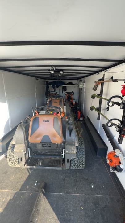 Enclosed trailer with a stand-on mower and trimmers racked inside