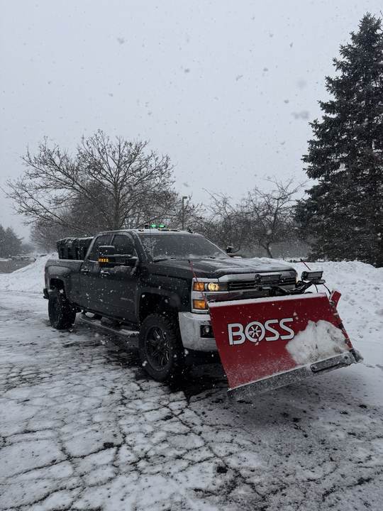 Pickup truck with a red snow plow during a snowfall